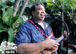 A Male Polynesian musician playing the ukulele in a tropical garden.