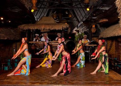 Five female Polynesian Dancers pose in a stylized pose wearing colorful traditional attire.