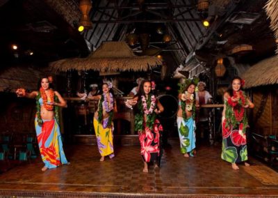 Five female Polynesian Dancers caught in mid-dance wearing colorful traditional attire.