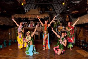 Five female Polynesian Dancers wearing colorful traditional attire with arms extended in a beautiful group pose.