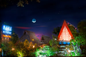 Gorgeous night view of the brightly lit Mai-Kai gardens and thatched roofs against the backdrop of stars and crescent moon.