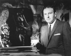 Vintage black and white photograph of Mr Thornton with glass next to Polynesian velvet painting.